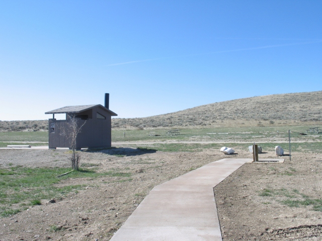 picture showing Toilet and water hydrant near the group picnic shelter. The water hydrant has a paved pathway, but access route to the toilet is along the road. There is also marked accessible parking next to the toilet.